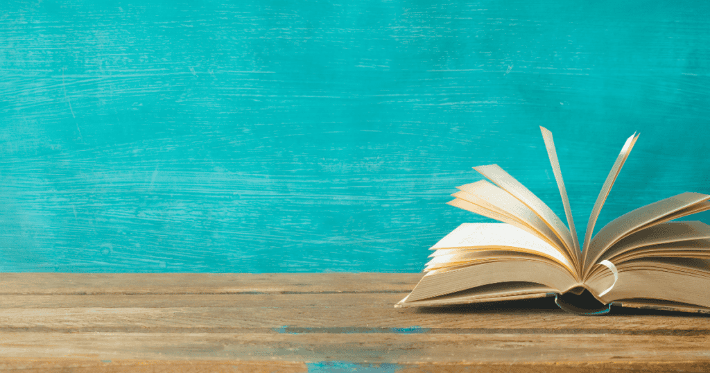 An open book with its pages fanned out rests on a wooden surface, set against a bright turquoise background—the perfect scene for discovering the best binge eating books.