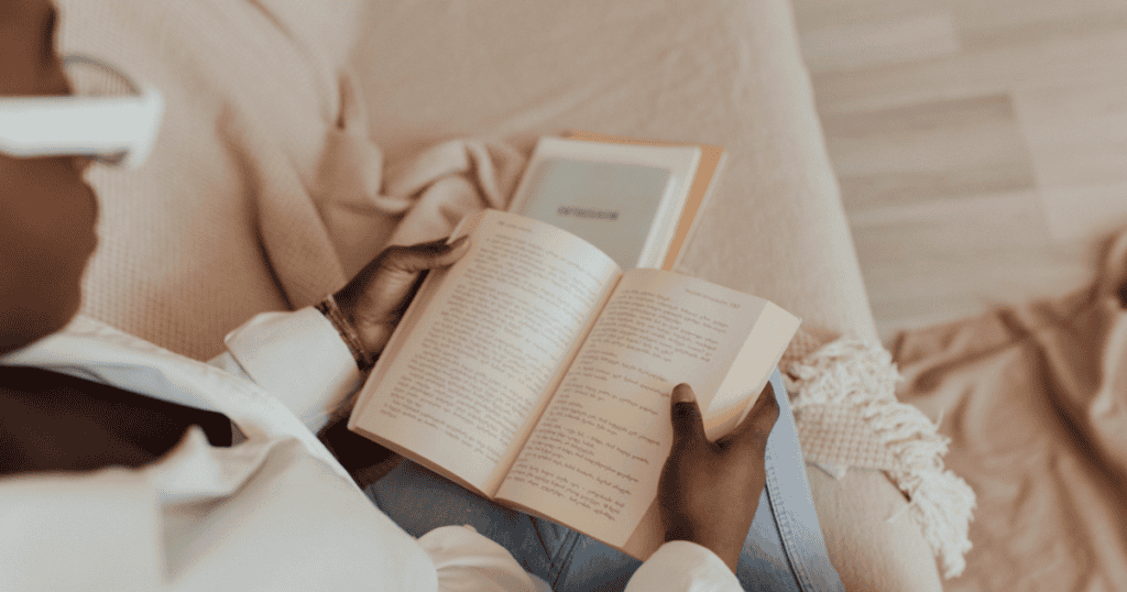 A person sitting on a couch reads an open book, with another closed book on food addiction resting nearby on a beige blanket.