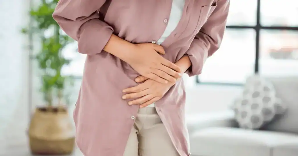 Person standing indoors, holding their stomach with both hands, appearing to be in pain or discomfort—highlighting the challenges of managing gastritis with nutrition.