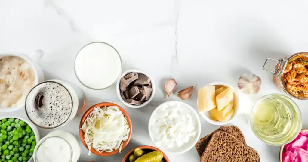 Assorted probiotic-rich foods on a white surface, including yogurt, kefir, sauerkraut, kimchi, cottage cheese, bread, pickles, peas, and garlic—beautifully displayed in bowls and jars—highlight the delicious variety found when comparing probiotics vs prebiotics in supporting gut health.