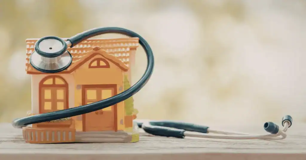 A toy house with a stethoscope draped around it, symbolizing home healthcare or medical care at home—highlighting the importance of monitoring weight and blood sugar health for families—rests on a wooden surface with a blurred background.