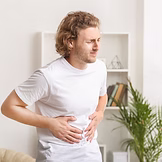 Man in white t-shirt satnding with hands on belly experiencing abdominal pain - gut health