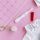 Positive pregnancy test with flower and calendar on pink desk