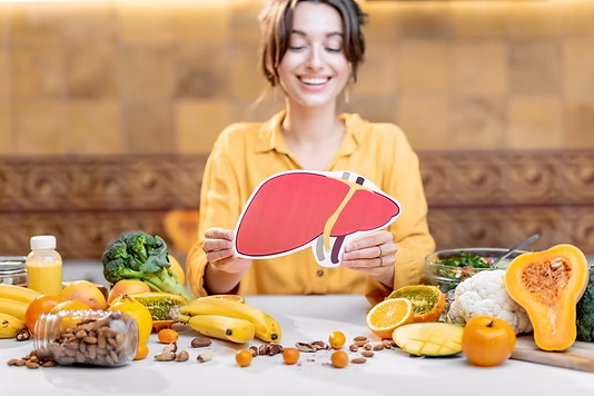 Liver Health & Fatty Liver, In good nutrition, Women sitting at a table with liver healthy fruits and vegetables and nuts on the table holding a healthy liver